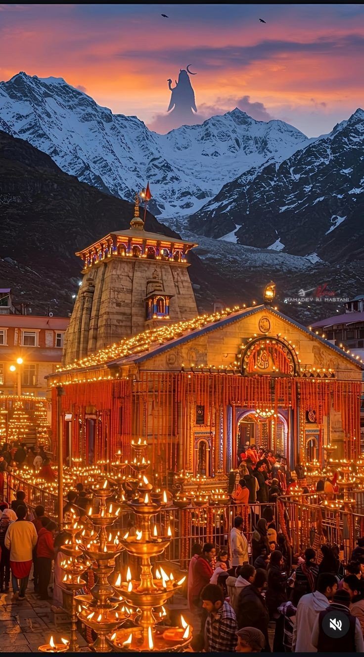 Kedarnath temple lit with lamps at sunset with snowy Himalayan peaks and a faint Shiva silhouette in the sky
